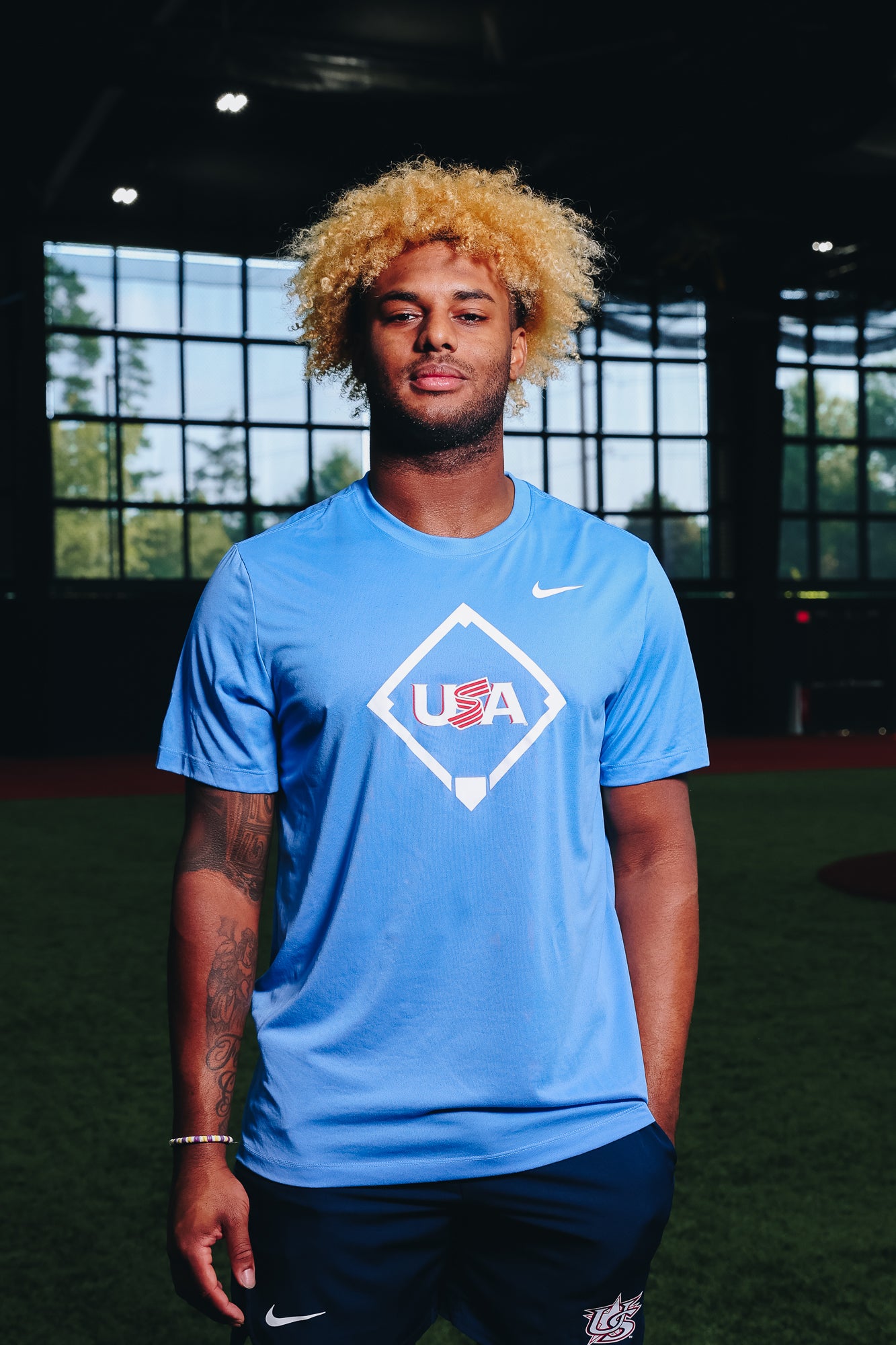 Male model wearing the Light Blue Home Plate Legend Tee featuring the USA Baseball Jersey logo in the Indoor Training Facility