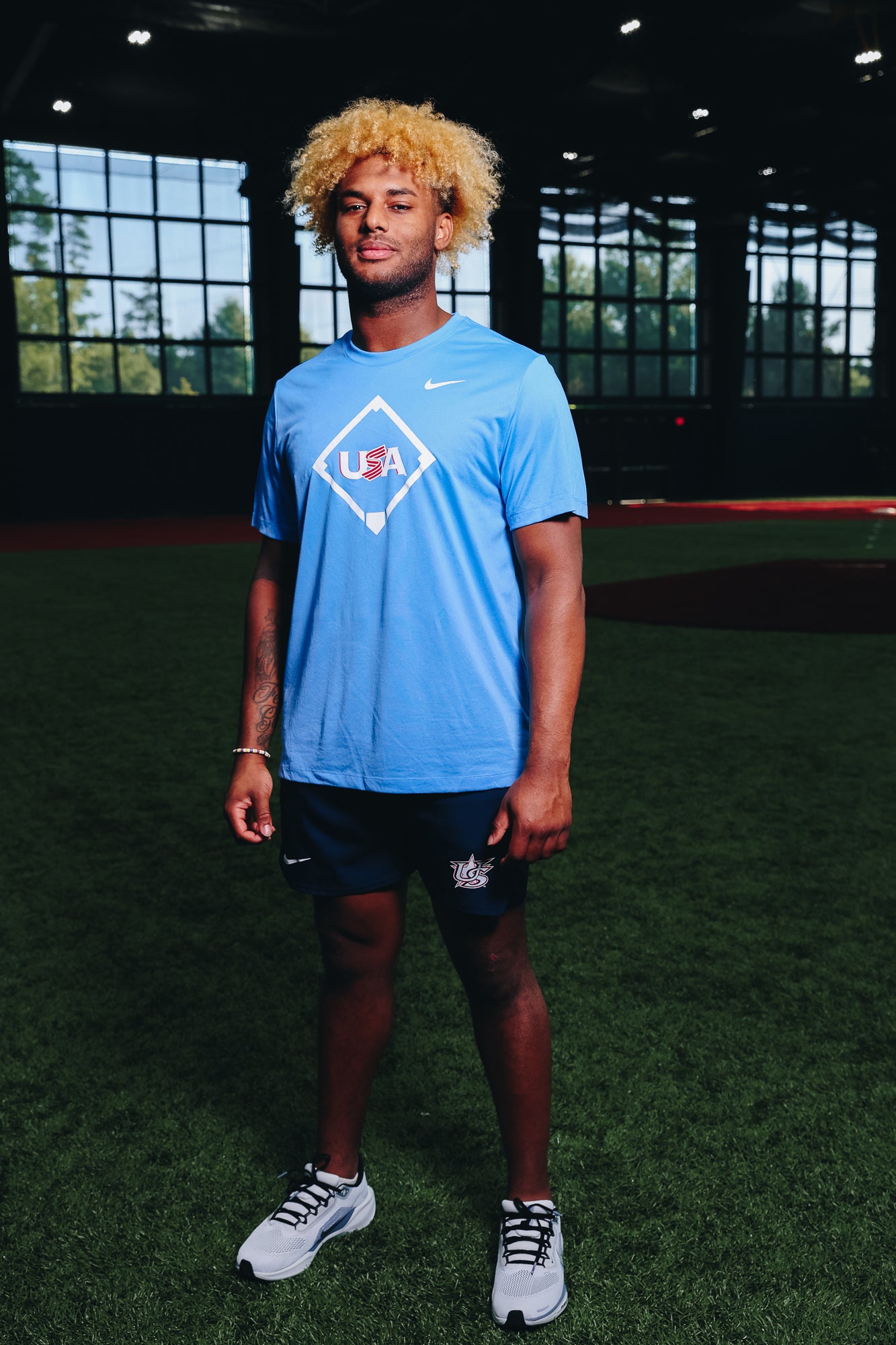 Male model wearing the Light Blue Home Plate Legend Tee featuring the USA Baseball Jersey logo in the Indoor Training Facility