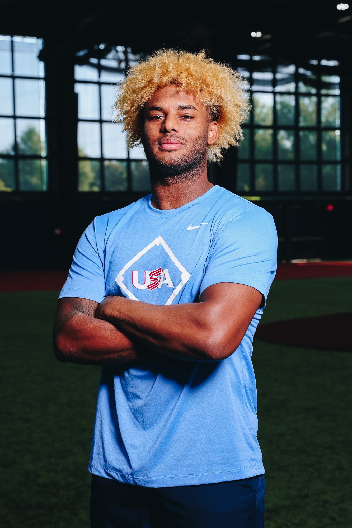 Male model wearing the Light Blue Home Plate Legend Tee featuring the USA Baseball Jersey logo in the Indoor Training Facility