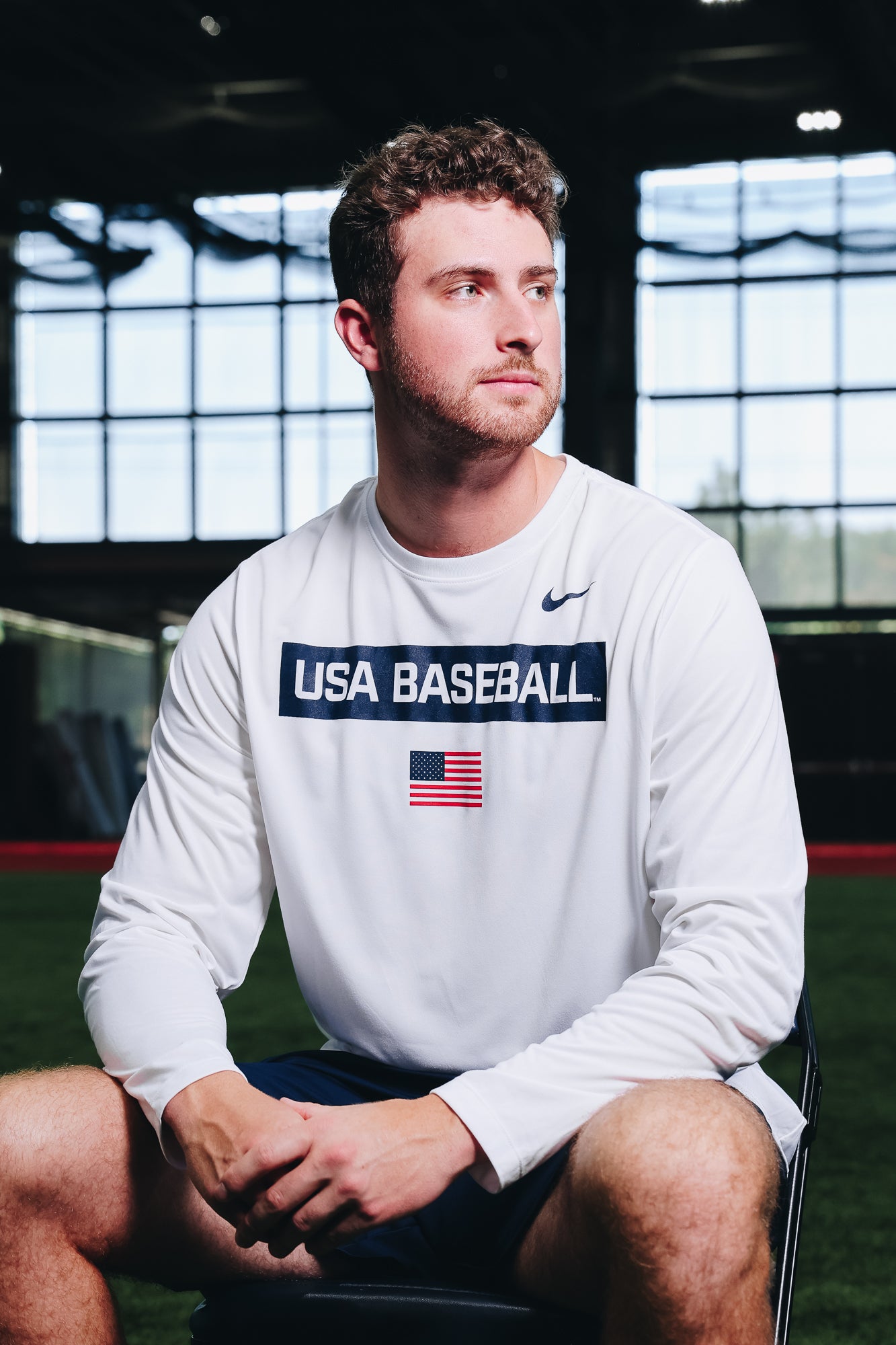 Male model wearing the White Defined Long Sleeve Legend Tee featuring the screen-printed American flag logo in the Indoor Training Facility