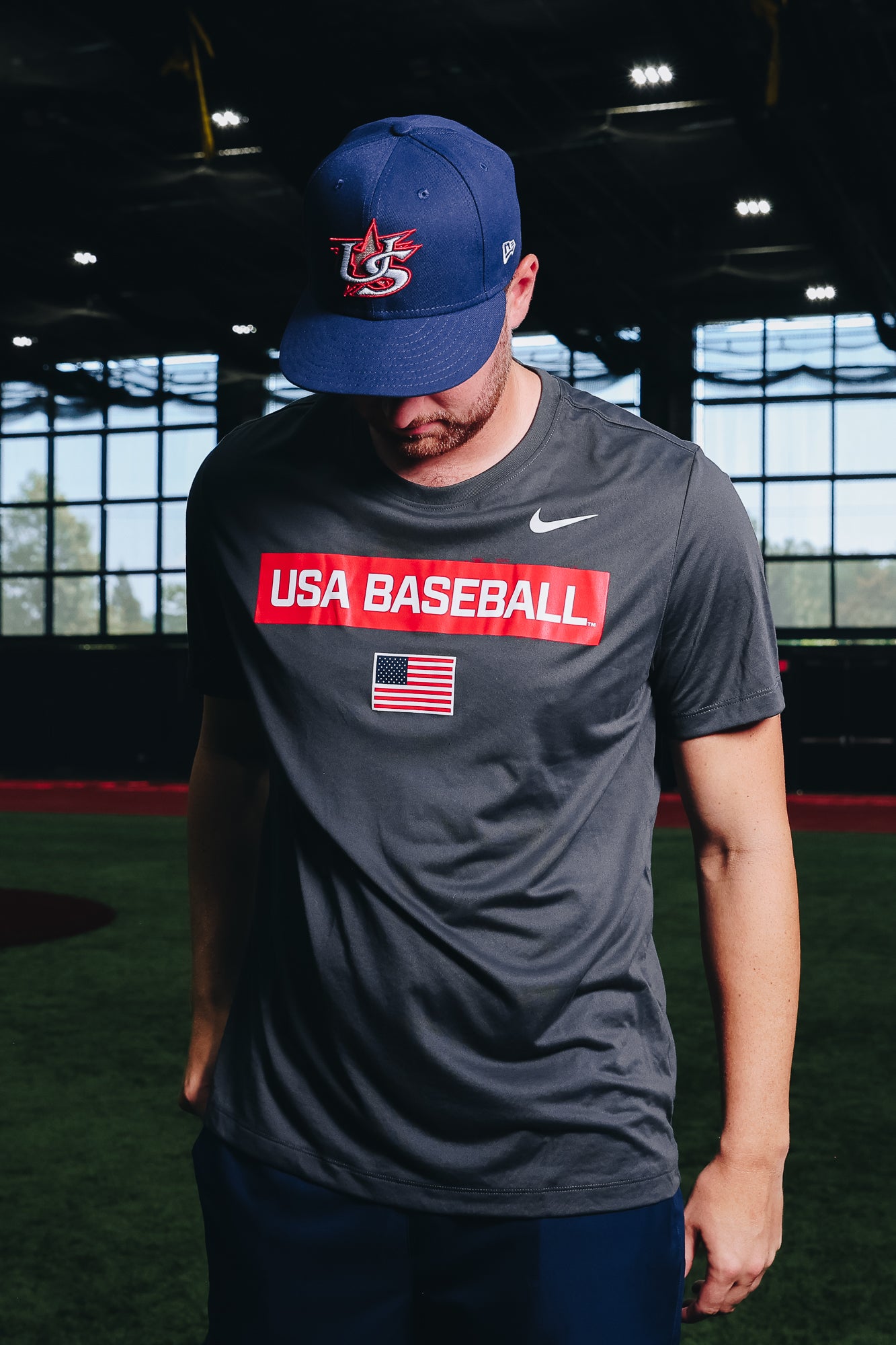 Male model wearing the USA Baseball Home Game Cap 59FIFTY and the Anthracite Defined Legend Tee featuring the screen-printed American flag logo in the Indoor Training Facility