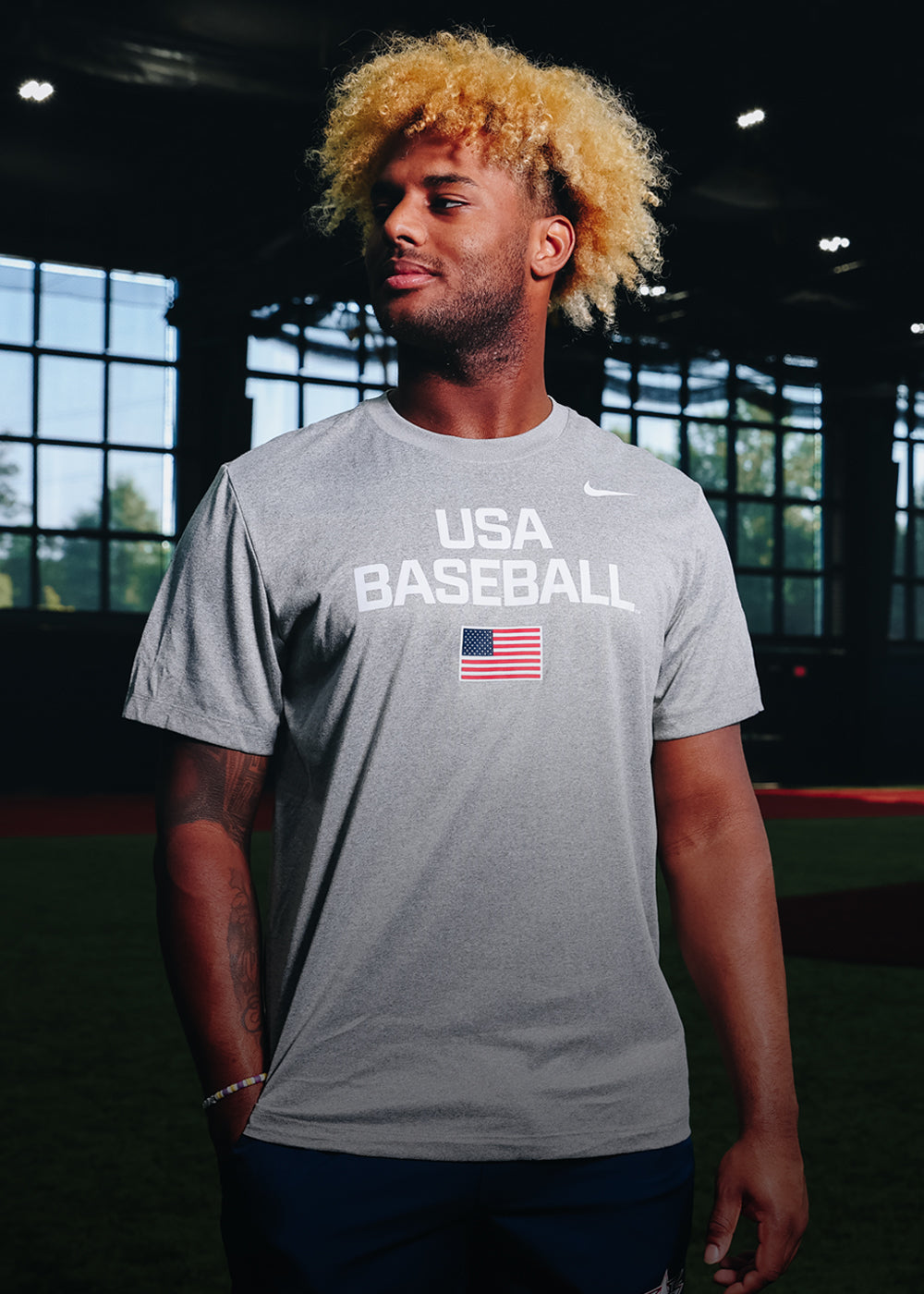 Person wearing a gray USA Baseball dynamic t-shirt with an American flag indoors.