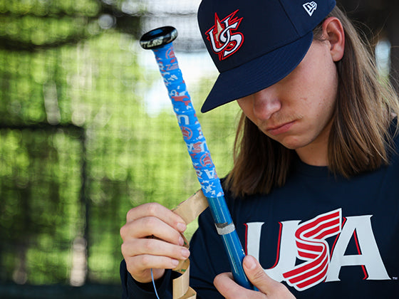 Male model applying VukGripz Bat Grip Tape, Blue Camo, wearing the Classic Jersey Logo Navy Long Sleeve Legend Tee, and Home Game Cap 59FIFTY.