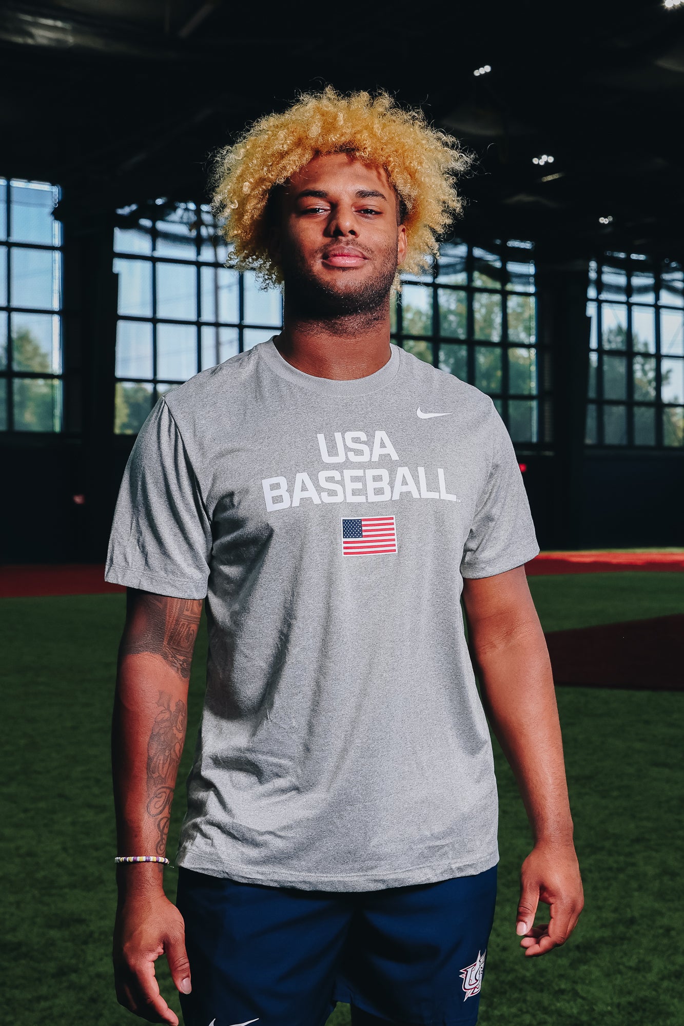 Male model wearing the Heather Grey Dynamic Legend Tee featuring the screen-printed American flag logo in Indoor Training Facility